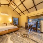 Rustic bedroom with a log frame bed warm lighting and exposed wooden ceiling beams marble floor and a seating table by the window
