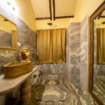 Luxurious marble bathroom with a carved wooden vessel sink a small statue washing a face beige curtains and a large mirror