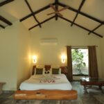 Cozy bedroom with a vaulted beamed ceiling a white bed centered with swan towel decor spelling LOVE warm wall lamps and green cushions by a window with brown curtains