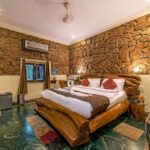 Rustic master bedroom with a large carved wooden bed against a stone wall white bedding and red throw pillows in a cozy hotel suite