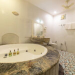 Spacious bathroom with a circular marble topped jacuzzi tub in the foreground pebble pattern floor and sink with mirror in the background