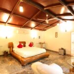 Rustic bedroom with a large carved wooden bed white bedding red pillows marble floor and warm ceiling lighting under a wooden beam ceiling