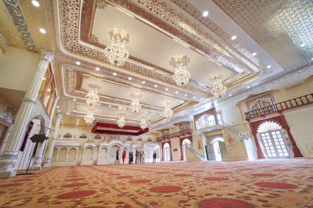 Luxurious ballroom with crystal chandeliers ornate ceilings and a red patterned carpet a small group of people gathers in the distance near arches and staircases