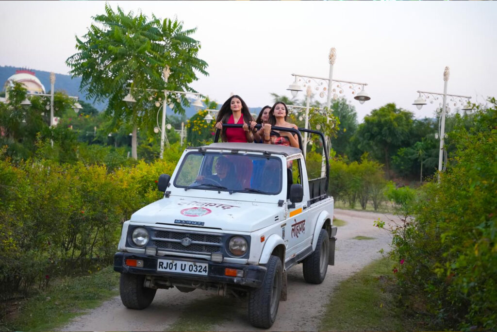 White open top jeep carrying people standing in the back riding along a dirt road through a green park like area with trees and decorative street lamps in the background