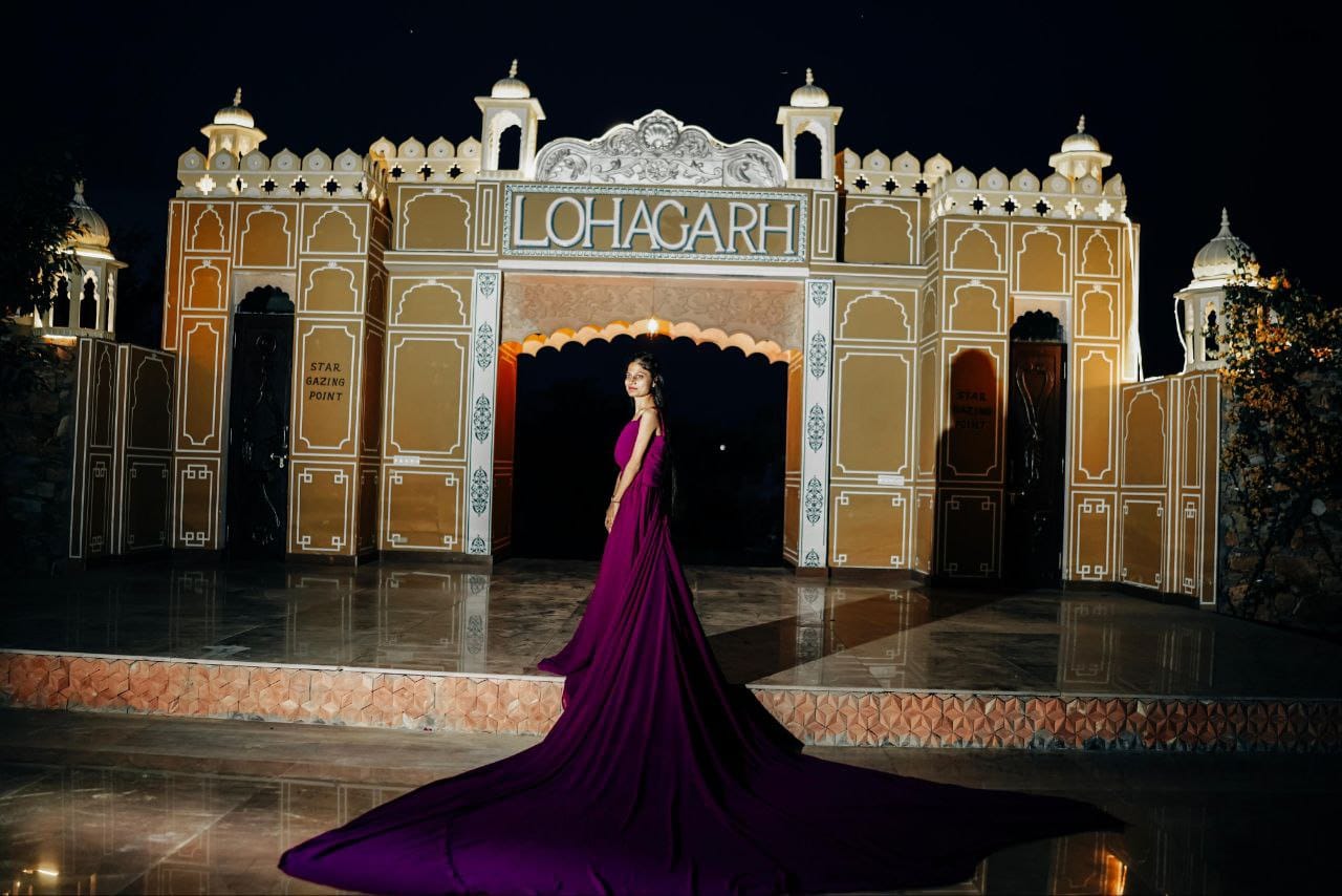 Nighttime view of an ornate Lohagarh gate with a woman in a magenta gown standing in front of it under the archway.